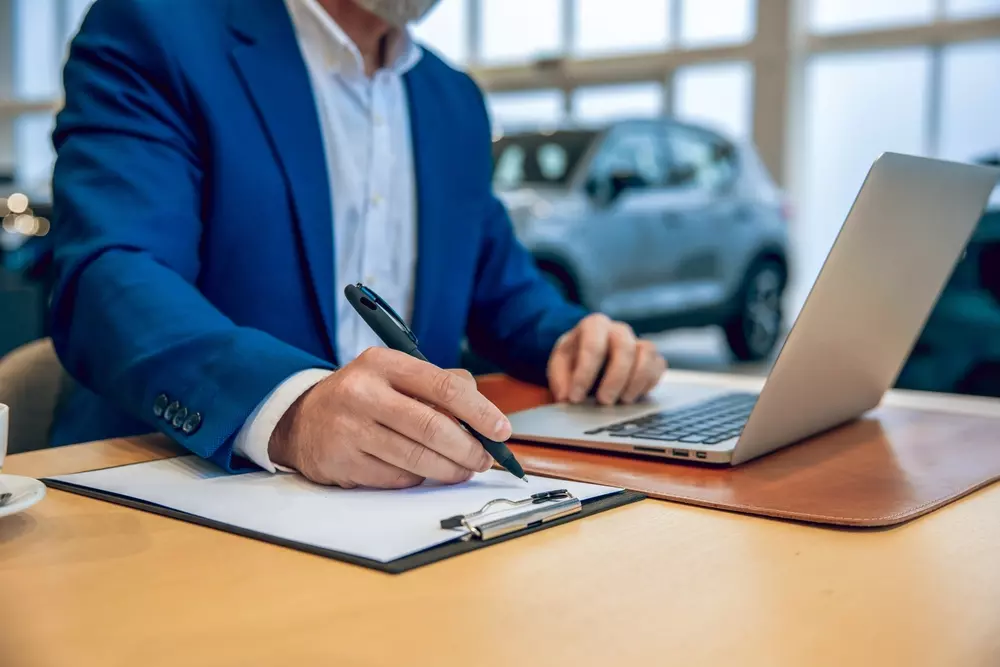 Unkenntlich gemachter Mann in einem Autohaus, trägt Anzug und arbeitet am Laptop