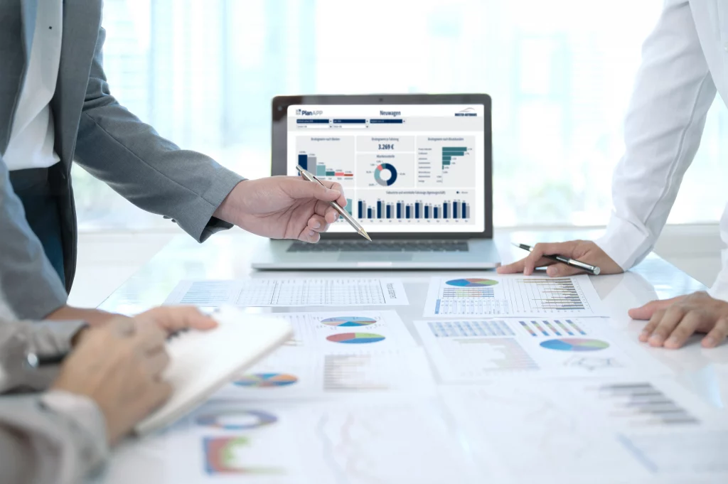Businessgespräch im Konferenzraum mit Kennzahlenanalyse und Laptop mit geöffneter PlanApp Power BI Grafik