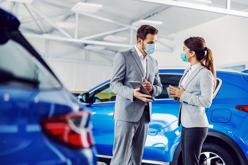 Autohändler und Kundin mit Coronamasken im Beratungsgespräch