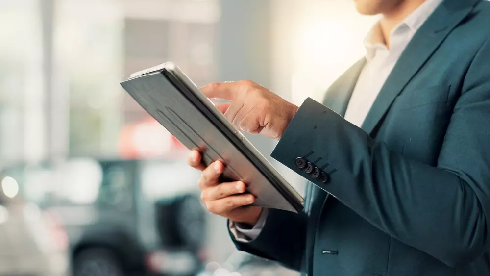 Geschäftsmann scrollt auf einem Tablet und liest Informationen für ein Autohaus