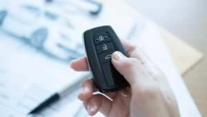 Hand hält Autoschlüssel-Fernbedienung vor verschwommenem Hintergrund mit Dokumenten