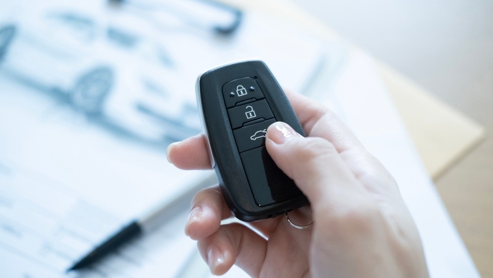 Hand hält Autoschlüssel-Fernbedienung vor verschwommenem Hintergrund mit Dokumenten